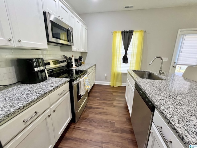 kitchen featuring white cabinetry, appliances with stainless steel finishes, decorative backsplash, light stone counters, and sink