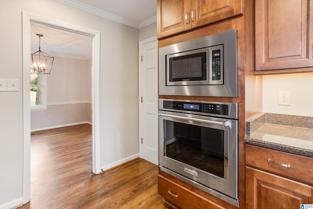 kitchen with crown molding, appliances with stainless steel finishes, brown cabinetry, wood finished floors, and dark stone counters