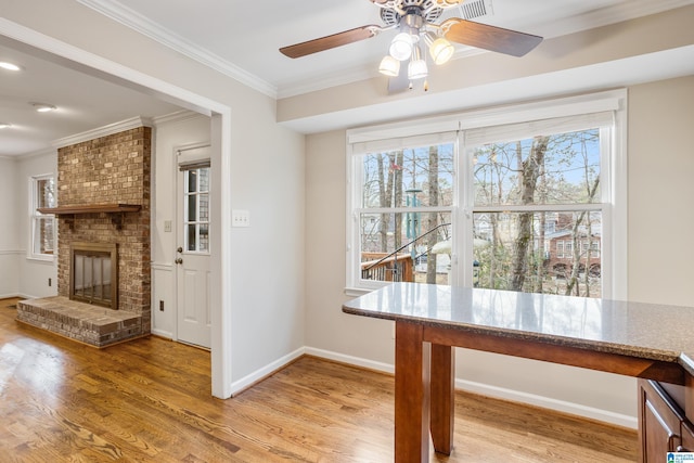 dining space with ornamental molding, a wealth of natural light, a brick fireplace, and wood finished floors