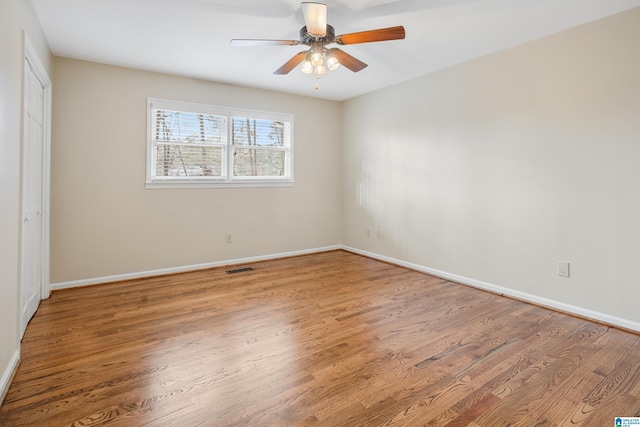 empty room with ceiling fan, wood finished floors, visible vents, and baseboards