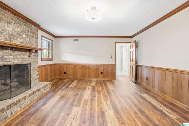 unfurnished living room with a wainscoted wall, crown molding, a textured ceiling, and wood finished floors