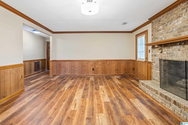 unfurnished living room with a brick fireplace, dark wood-type flooring, a textured ceiling, and wainscoting