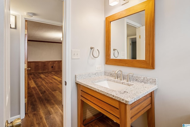 bathroom with a wainscoted wall, wood finished floors, crown molding, vanity, and wood walls