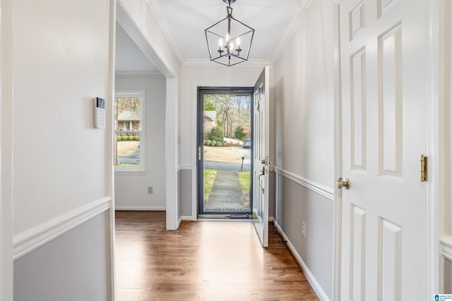 foyer entrance with baseboards, ornamental molding, a chandelier, and wood finished floors