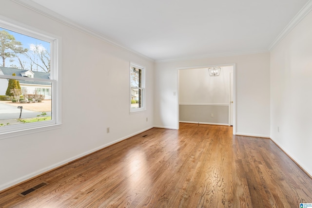 spare room featuring baseboards, visible vents, wood finished floors, an inviting chandelier, and crown molding