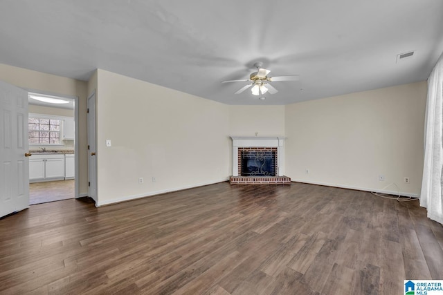 unfurnished living room featuring a brick fireplace, dark wood-type flooring, sink, and ceiling fan