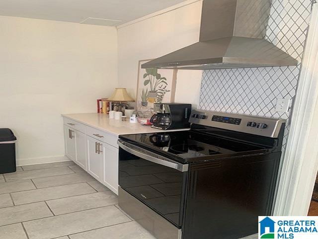 kitchen featuring wall chimney exhaust hood, white cabinets, and electric range