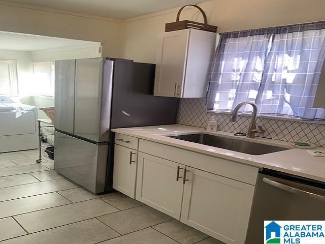 kitchen with stainless steel dishwasher, white cabinets, sink, and tasteful backsplash