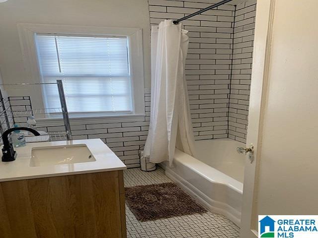 bathroom featuring tile patterned flooring, shower / bathtub combination with curtain, vanity, and tile walls