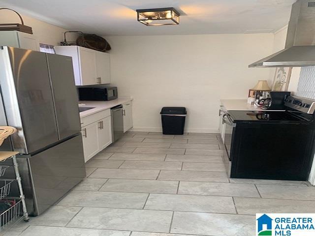 kitchen featuring stainless steel appliances, white cabinetry, and wall chimney range hood