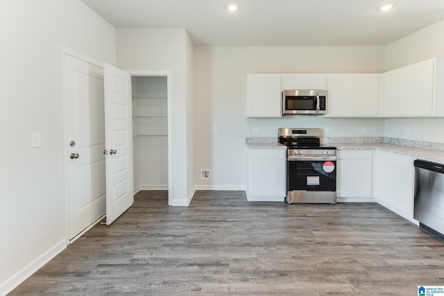 kitchen with light stone counters, white cabinetry, stainless steel appliances, and light wood-type flooring