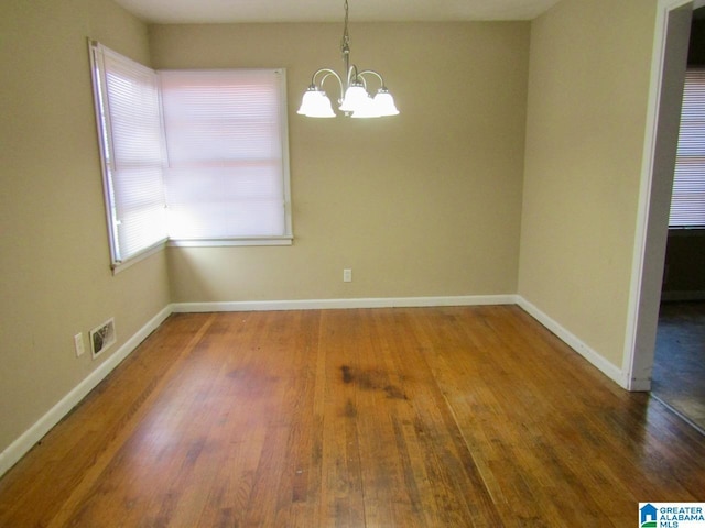 spare room with dark wood-type flooring and an inviting chandelier