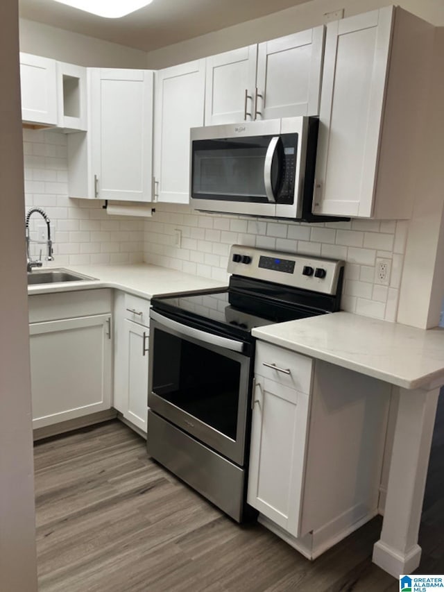 kitchen featuring white cabinets, appliances with stainless steel finishes, wood-type flooring, decorative backsplash, and sink