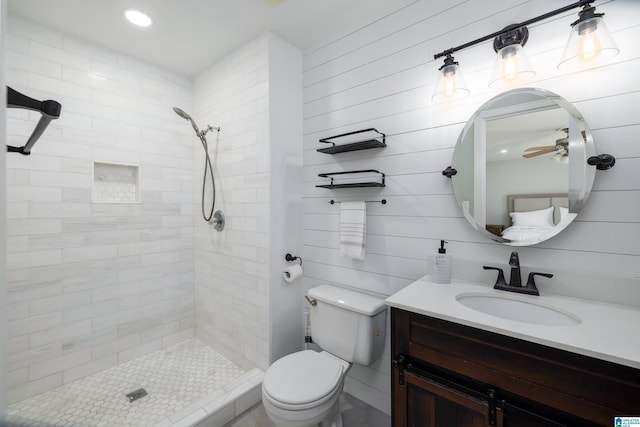 bathroom featuring ceiling fan, toilet, vanity, and a tile shower