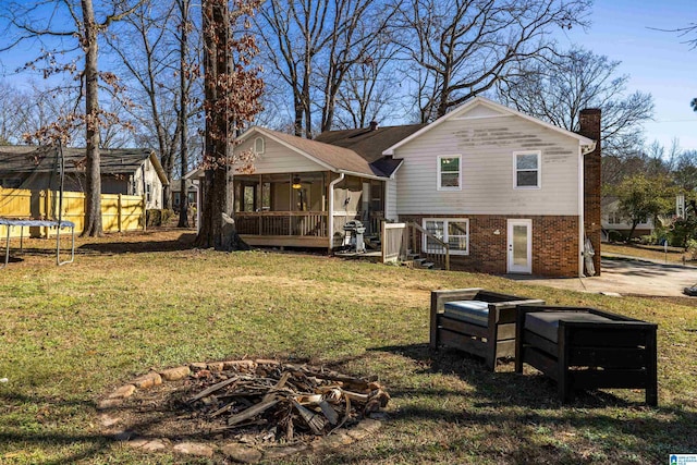 back of house featuring an outdoor fire pit, a trampoline, and a yard