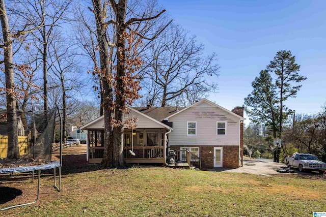 rear view of property with a trampoline, a yard, and a sunroom