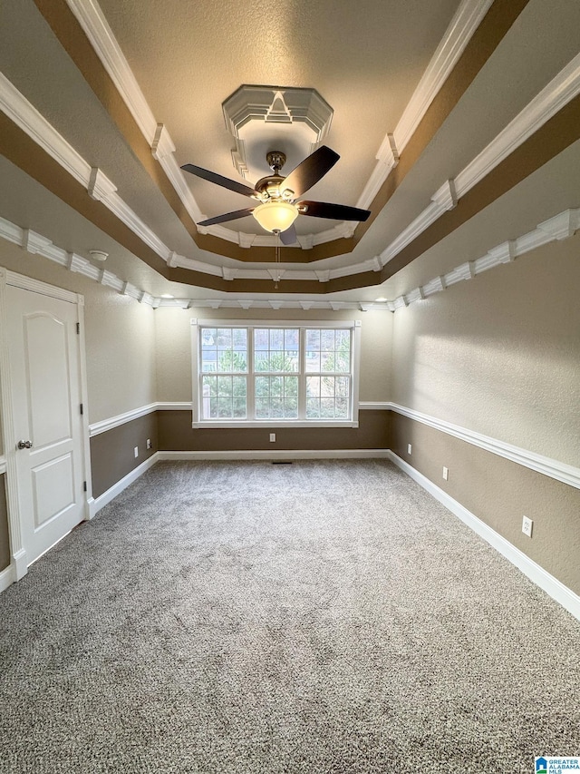 empty room with ceiling fan, ornamental molding, carpet floors, and a tray ceiling