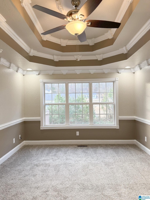 carpeted empty room with ceiling fan, crown molding, and a tray ceiling