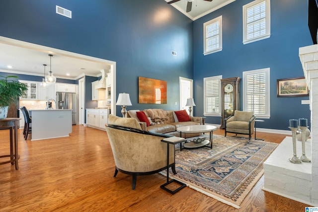 living room featuring light wood-type flooring, a towering ceiling, and crown molding