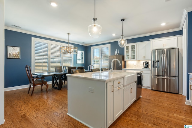 kitchen featuring decorative light fixtures, a center island with sink, white cabinets, and stainless steel appliances