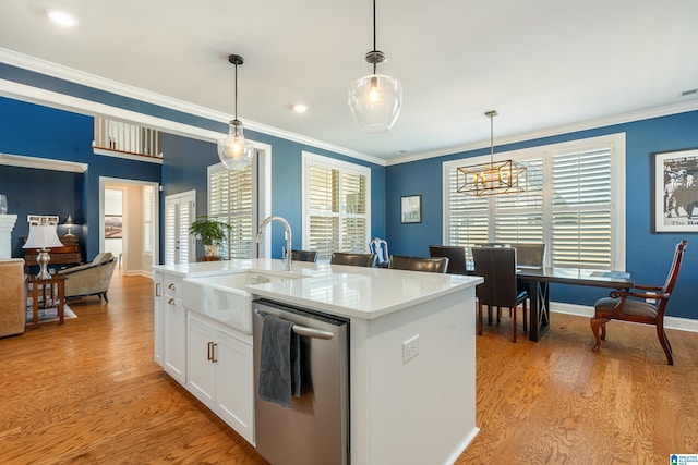 kitchen with hanging light fixtures, stainless steel dishwasher, white cabinets, ornamental molding, and a center island with sink