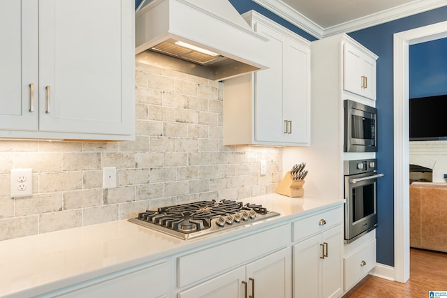 kitchen with white cabinets, stainless steel appliances, tasteful backsplash, premium range hood, and ornamental molding