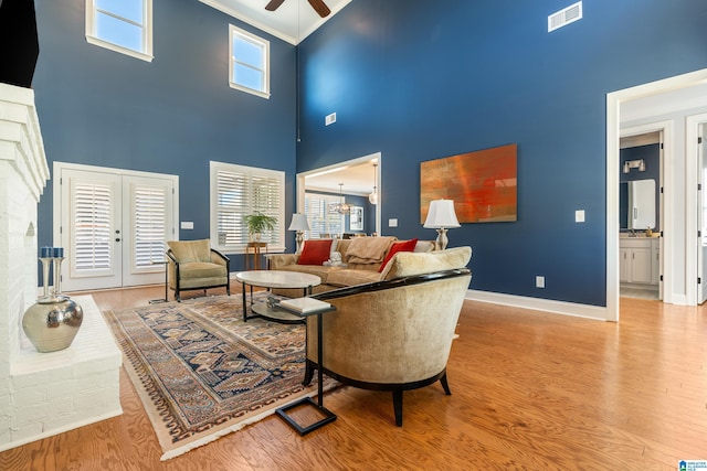 living room with ceiling fan with notable chandelier, a high ceiling, crown molding, and light wood-type flooring