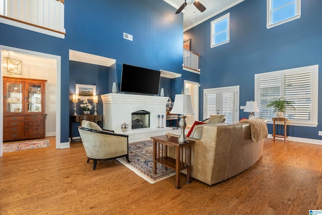 living room with a fireplace, wood-type flooring, a high ceiling, and crown molding