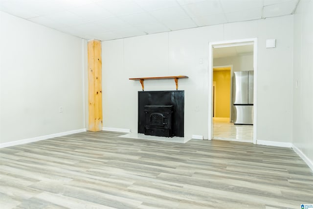 unfurnished living room with a paneled ceiling, a wood stove, and light hardwood / wood-style floors