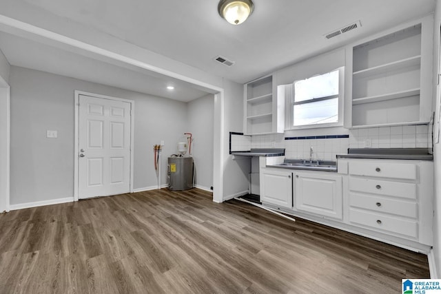 kitchen with white cabinetry, wood-type flooring, sink, backsplash, and electric water heater