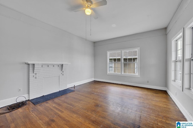 unfurnished living room featuring dark wood-type flooring, ceiling fan, crown molding, and a brick fireplace