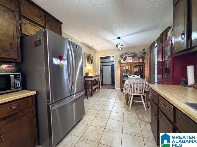 kitchen with a textured ceiling, light tile patterned floors, dark brown cabinetry, and appliances with stainless steel finishes