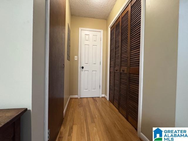 hall with light wood-type flooring and a textured ceiling