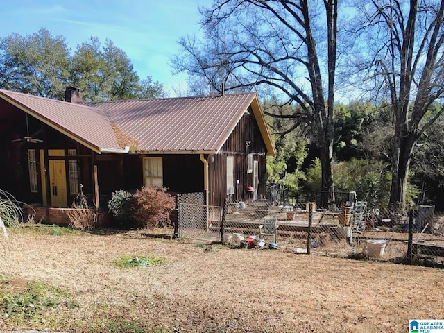 view of side of home featuring metal roof, a chimney, fence, and a ceiling fan