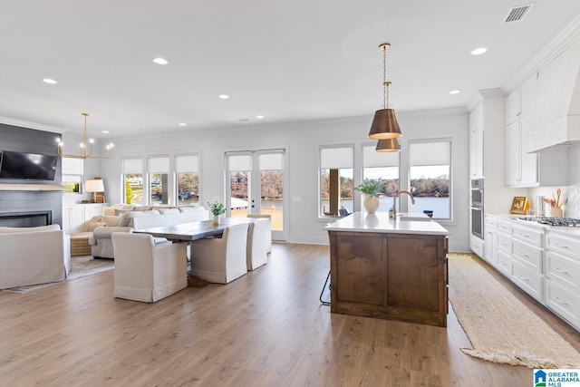 kitchen with white cabinetry, decorative light fixtures, and an island with sink