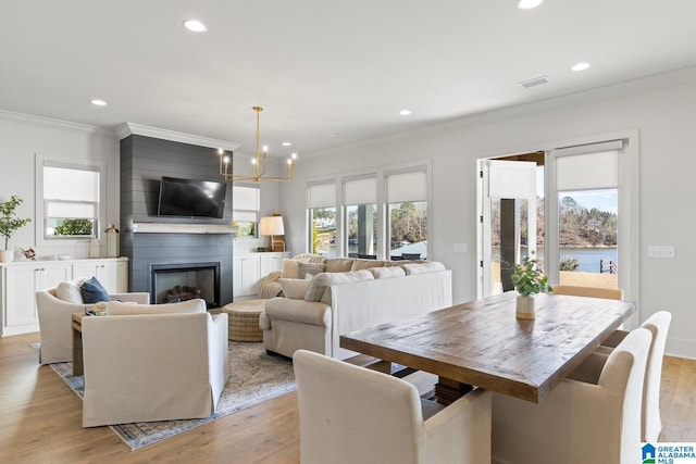 dining room with an inviting chandelier, a fireplace, crown molding, and light hardwood / wood-style flooring