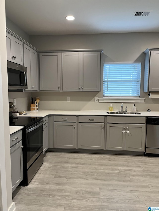 kitchen with light wood-type flooring, sink, gray cabinetry, and stainless steel appliances