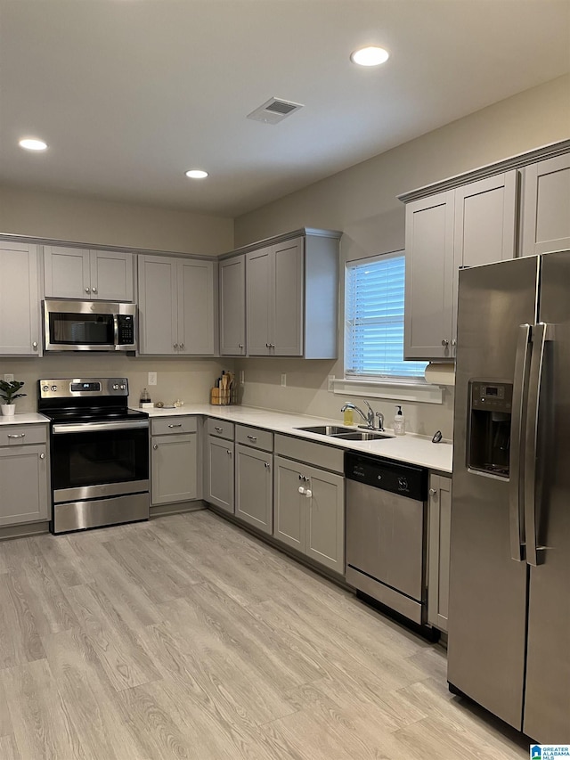 kitchen with sink, appliances with stainless steel finishes, gray cabinets, and light wood-type flooring