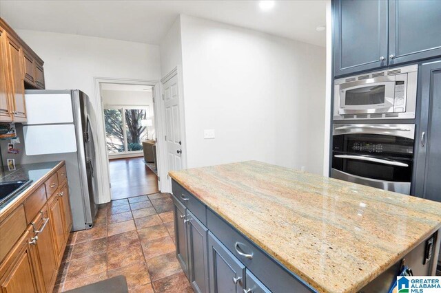 kitchen with stainless steel appliances, a kitchen island, light stone countertops, and gray cabinets