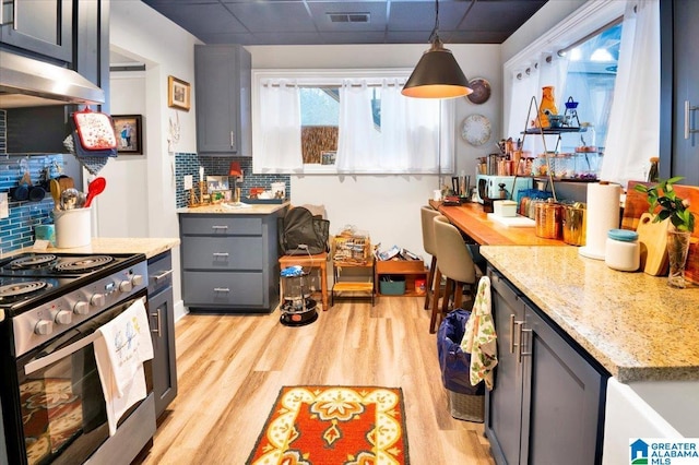 kitchen featuring electric stove, decorative backsplash, hanging light fixtures, and light hardwood / wood-style flooring