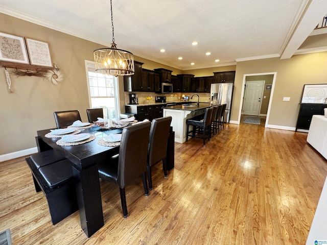 dining area featuring sink, light hardwood / wood-style flooring, ornamental molding, and an inviting chandelier