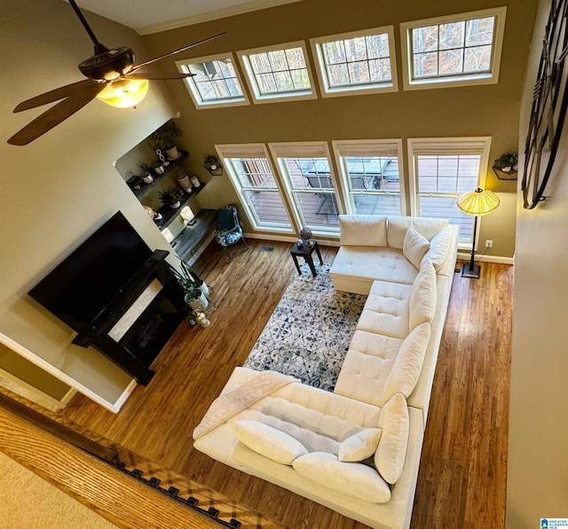 living room with ceiling fan, plenty of natural light, a towering ceiling, and hardwood / wood-style floors