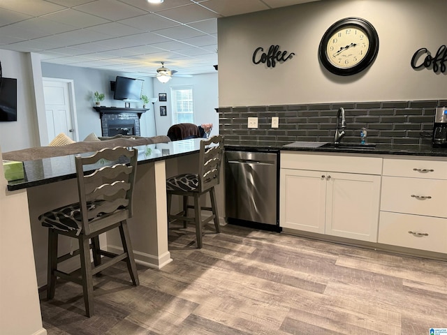 kitchen with stainless steel dishwasher, decorative backsplash, kitchen peninsula, sink, and white cabinetry