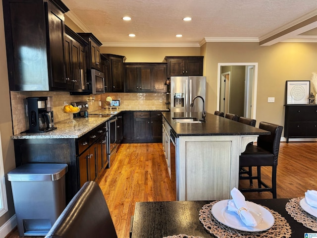 kitchen with appliances with stainless steel finishes, decorative backsplash, sink, light wood-type flooring, and a center island with sink