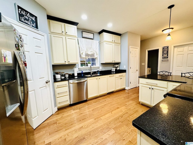 kitchen with light hardwood / wood-style flooring, appliances with stainless steel finishes, dark stone countertops, white cabinets, and sink