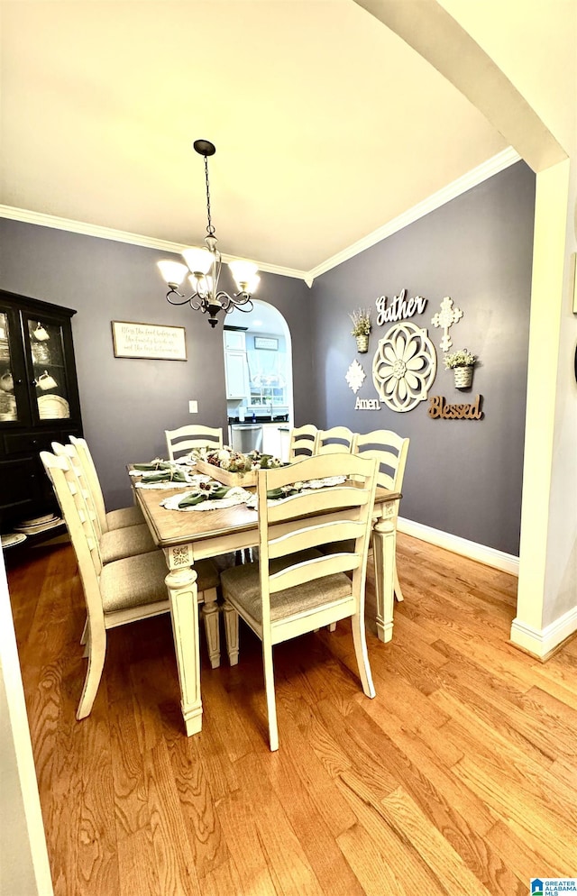 dining area with light wood-type flooring, an inviting chandelier, and crown molding