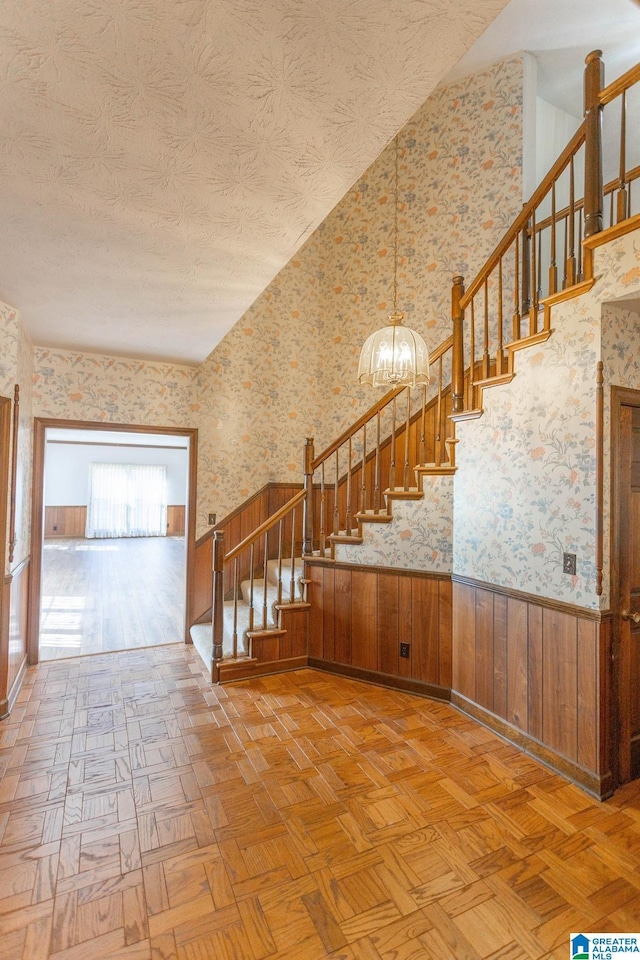 stairs with parquet flooring, a textured ceiling, and an inviting chandelier