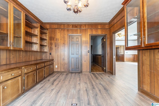 interior space featuring light wood-type flooring, a chandelier, crown molding, and wood walls