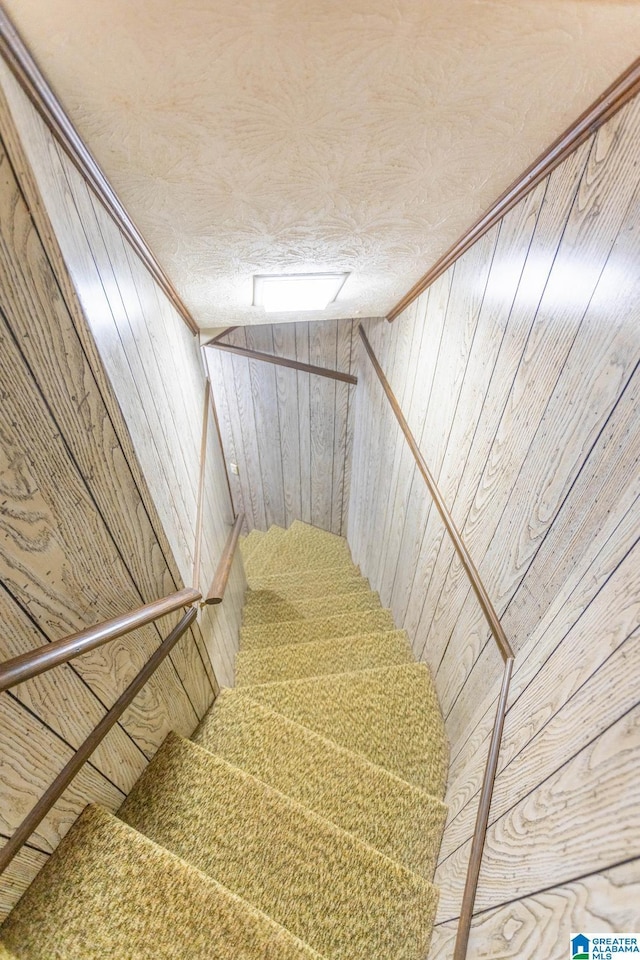 stairs featuring a textured ceiling, vaulted ceiling, and wooden walls