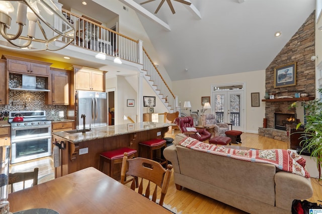 living room featuring a notable chandelier, sink, light hardwood / wood-style flooring, a stone fireplace, and high vaulted ceiling